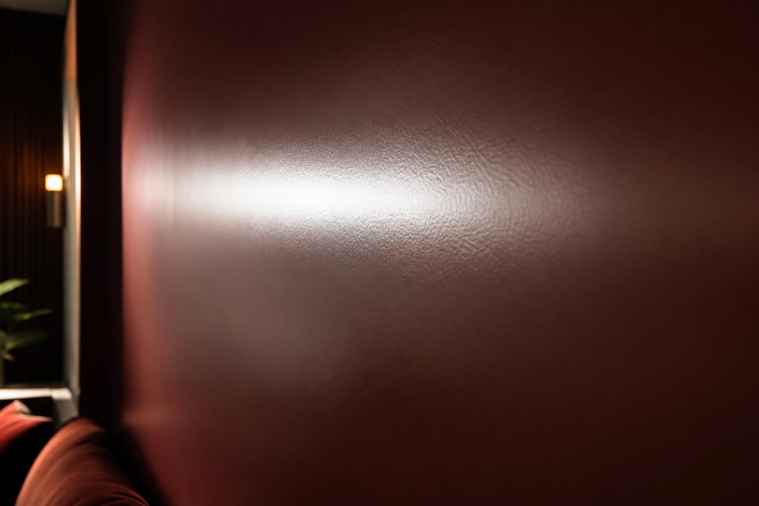 Deep Atelier shade satin feature wall with a luminous highlight band under raking sconce light